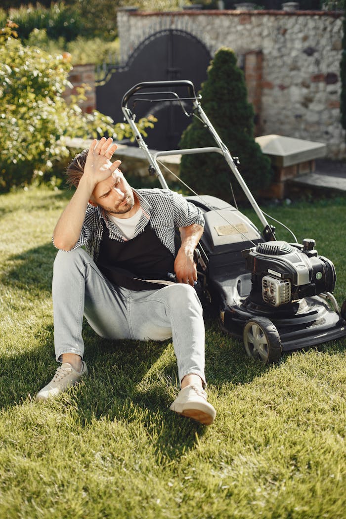 about-04 A tired man sitting on the grass with a lawn mower after gardening.